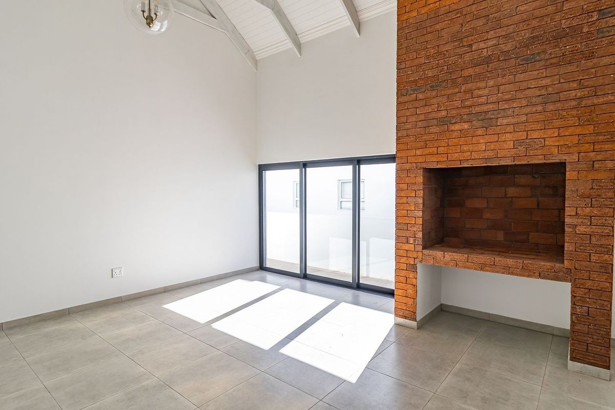 Spacious living area featuring a striking exposed brick fireplace, vaulted ceilings, and large sliding glass doors that provide ample natural light.