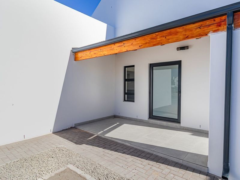 A clean, modern covered patio area featuring tiled flooring, a timber beam accent, and direct access to the exterior through an aluminium door.