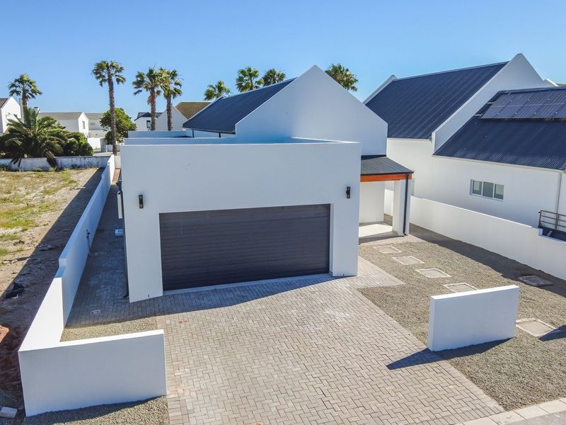 Aerial view of a modern house featuring a double garage, paved driveway, and clean white exterior finishes with solar panels on the roof.