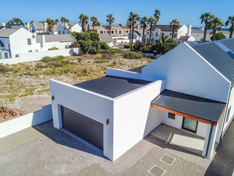 Aerial view of a modern white house featuring a double garage, paved driveway, and covered entrance within a residential estate setting.