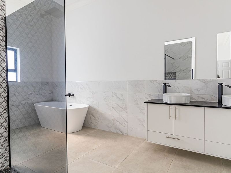 Modern, spacious bathroom featuring a double vanity with vessel sinks, a freestanding bathtub, and a large glass-enclosed shower with stylish feature tiling.