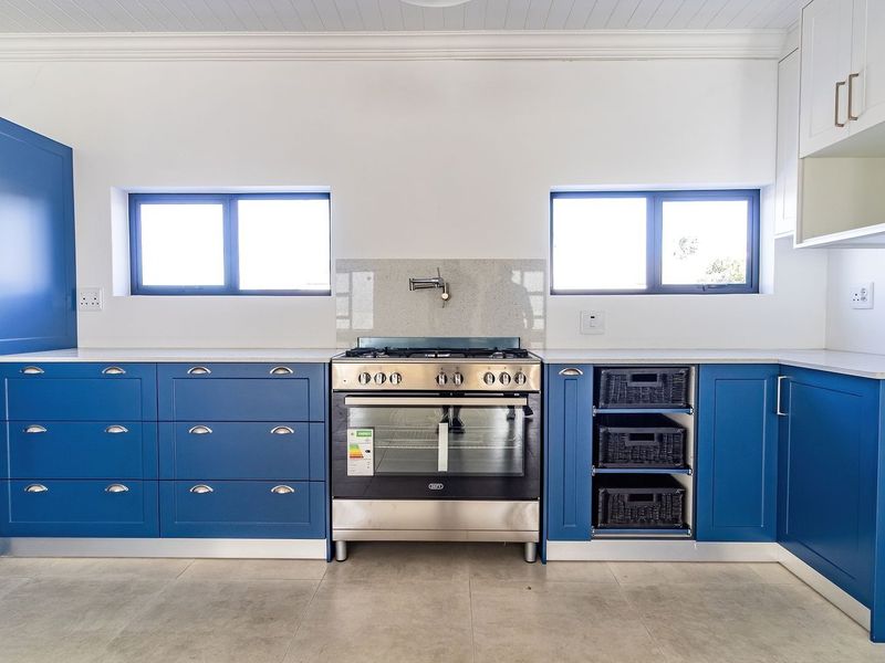 Modern kitchen featuring vibrant blue cabinetry, stone countertops, a stainless steel gas oven, and neutral tiled flooring in a clean, well-lit space.