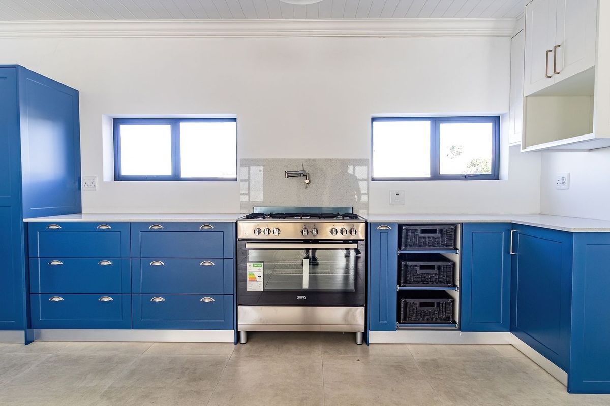 Modern kitchen featuring vibrant blue cabinetry, stone countertops, a stainless steel gas oven, and neutral tiled flooring in a clean, well-lit space.
