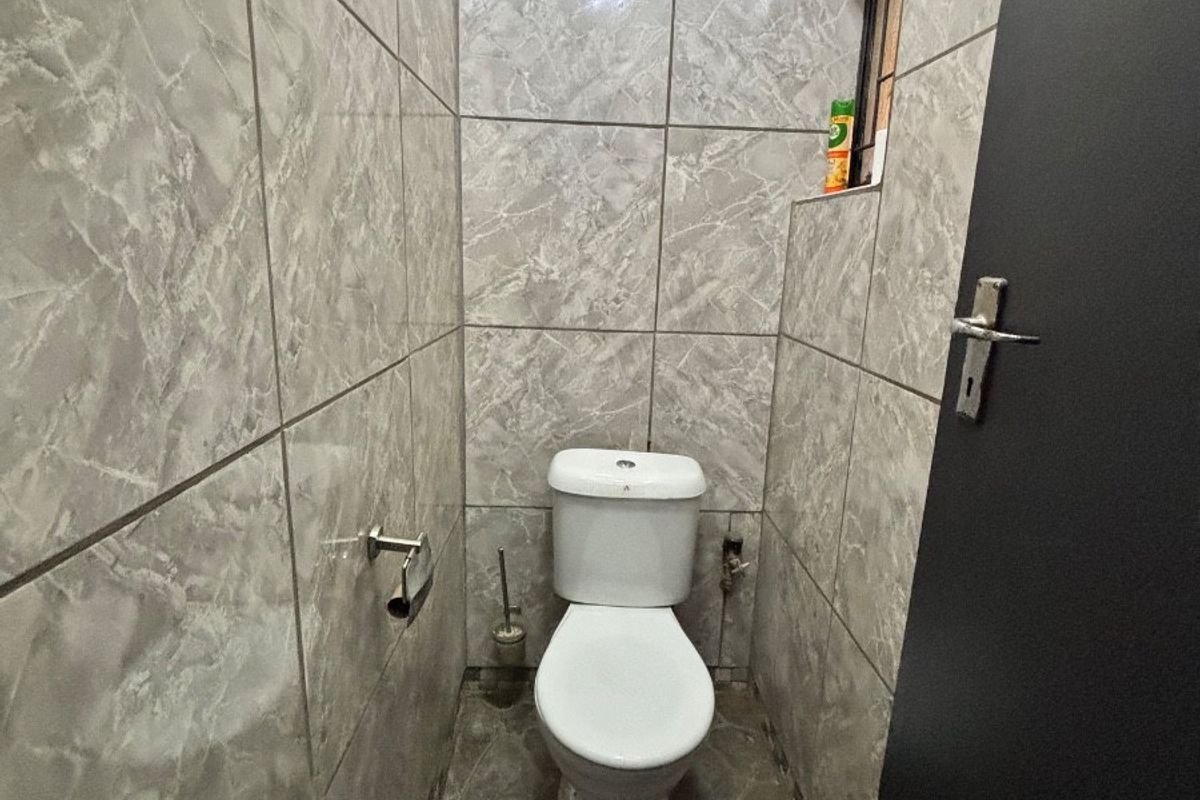 A compact guest bathroom featuring full-height marble-effect wall tiling and stone-look floor tiles, equipped with a standard white toilet.