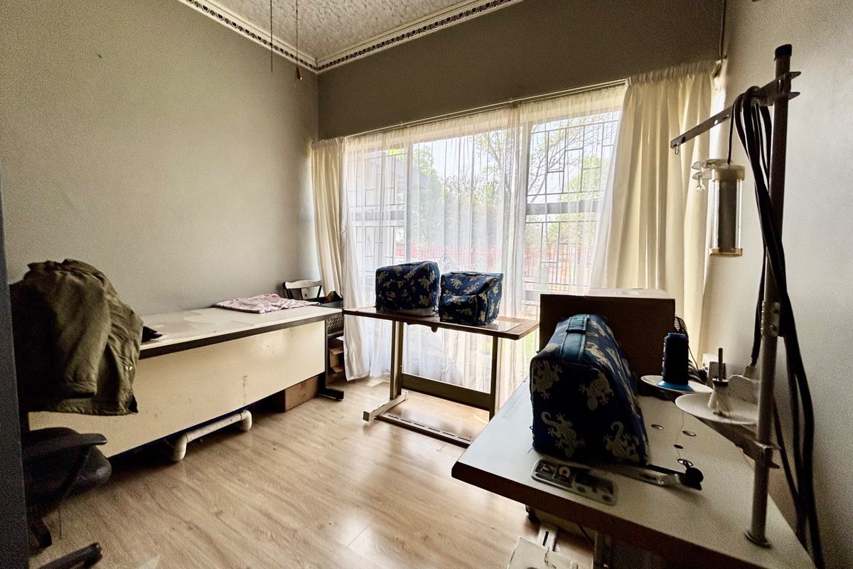 A bedroom space featuring laminate flooring and decorative ceiling cornicing, currently utilized as a workspace with security bars installed on the window.