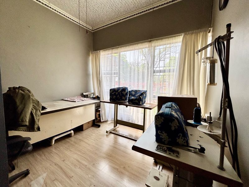 A bedroom space featuring laminate flooring and decorative ceiling cornicing, currently utilized as a workspace with security bars installed on the window.