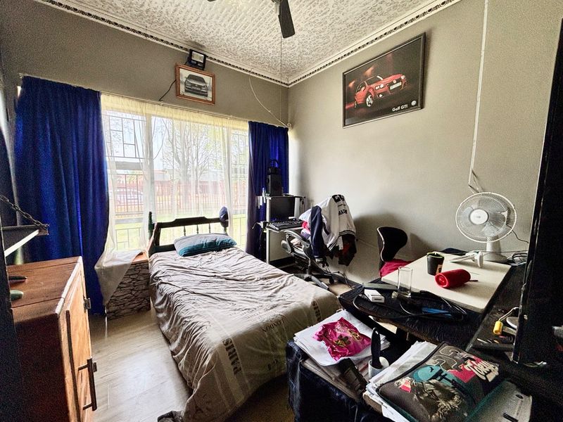 A bedroom featuring decorative ceiling molding, a ceiling fan, and large windows with security bars, requiring cosmetic updates to improve its overall condition.