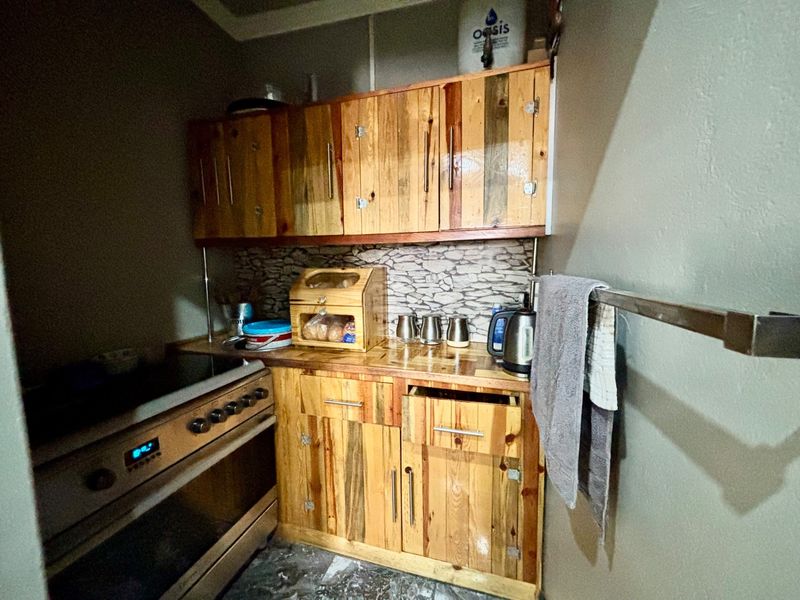 A compact kitchen area featuring custom wooden cabinetry, a stone-look backsplash, and a built-in electric oven and hob.