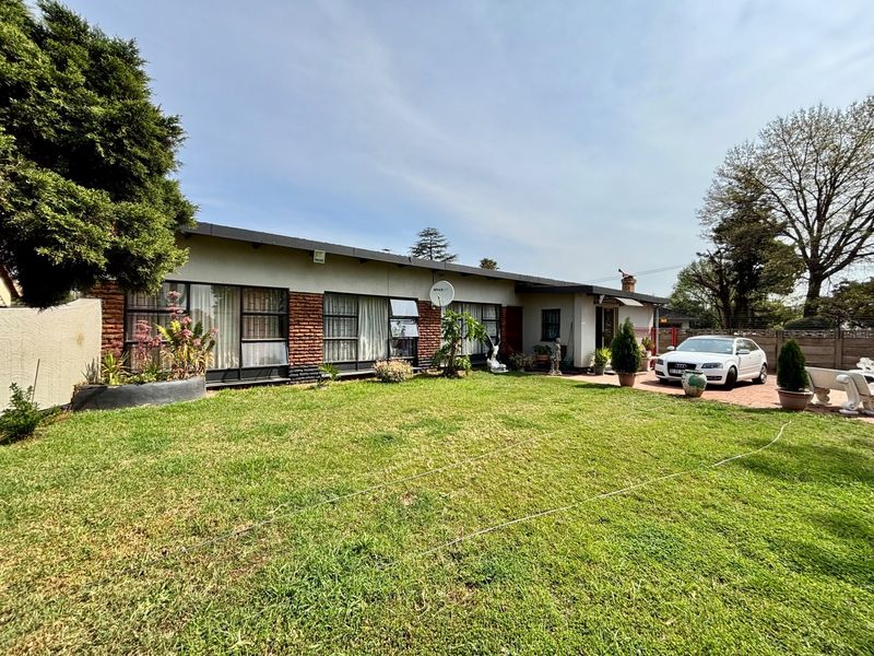 A rear view of a single-story house featuring a brick and rendered facade, large windows, and a spacious lawn area.