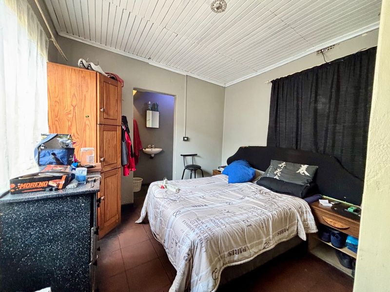 A bedroom featuring tiled flooring, a tongue and groove ceiling, and an attached en-suite area with a basin.
