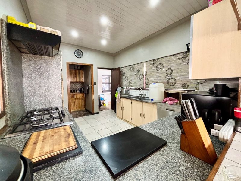 A functional kitchen featuring granite countertops, a gas hob with extractor fan, built-in cabinetry, and tiled flooring, leading to a secondary utility area.