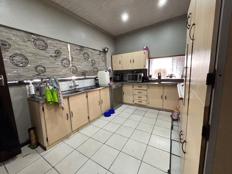 A functional kitchen featuring laminate cabinetry, tiled flooring, and a double stainless steel sink with a tiled backsplash.