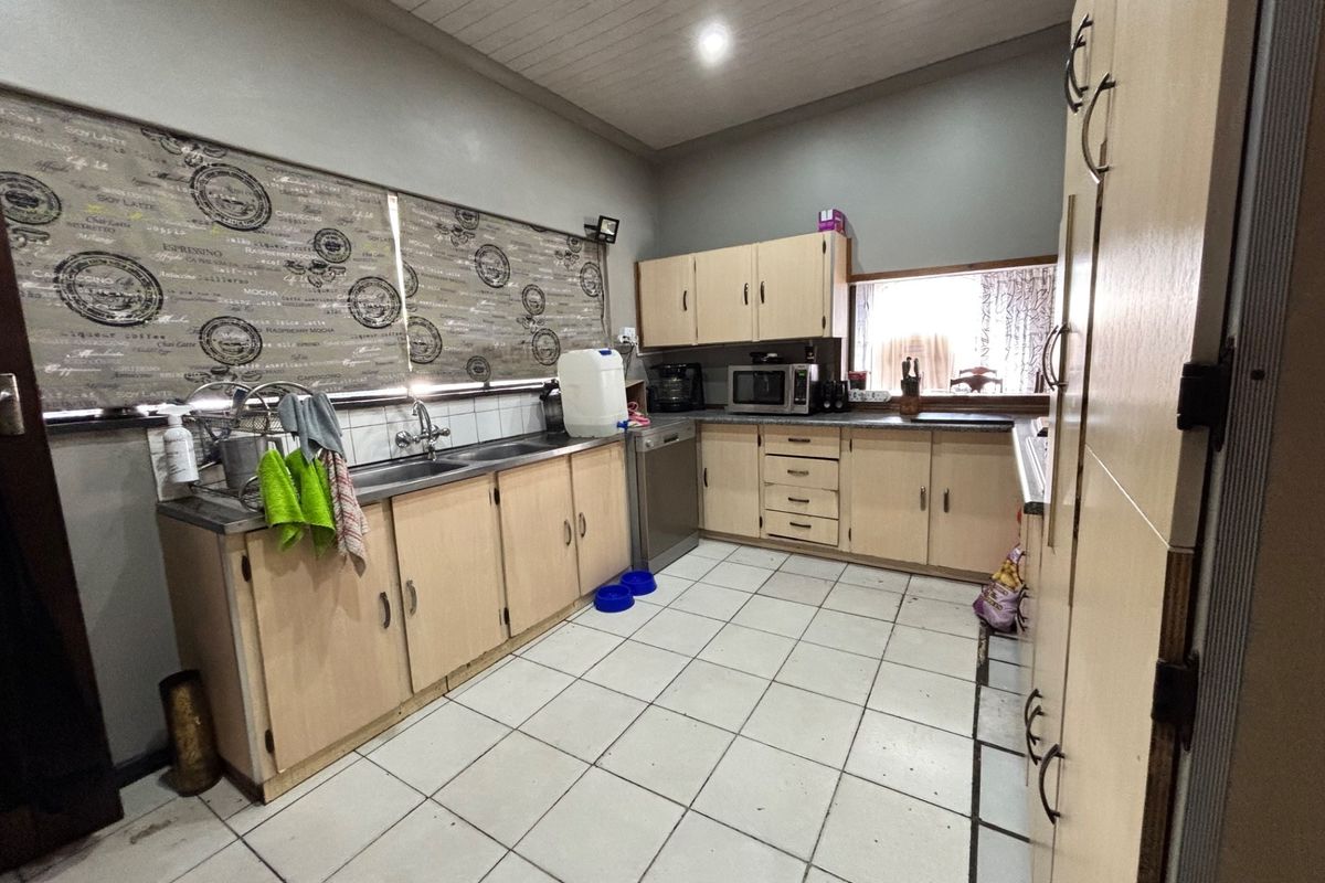 A functional kitchen featuring laminate cabinetry, tiled flooring, and a double stainless steel sink with a tiled backsplash.