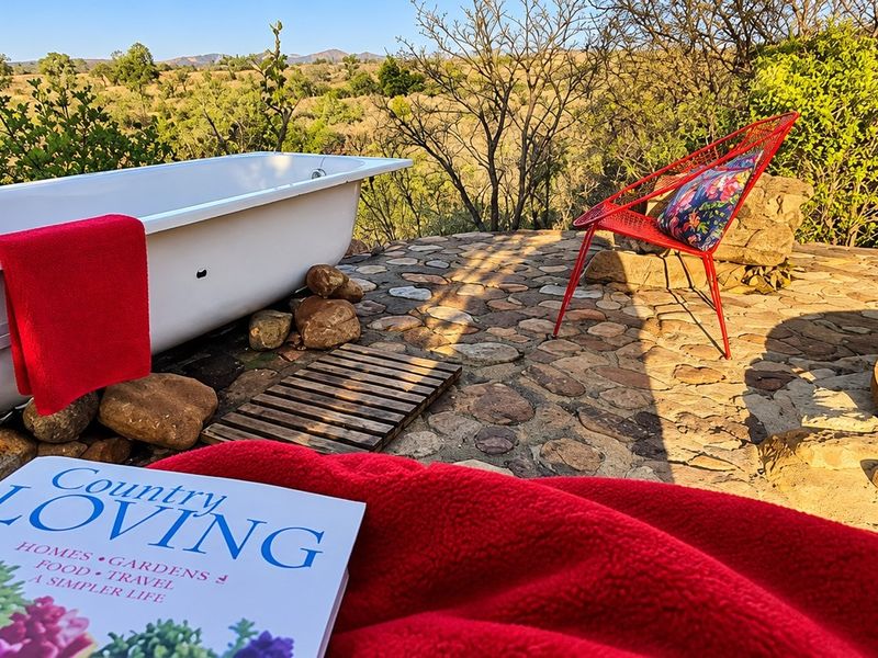 An outdoor patio area featuring a freestanding bathtub set on a stone-paved surface with scenic natural views.