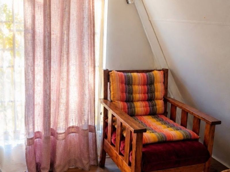 A cozy attic-style bedroom featuring sloped ceilings, laminate flooring, and natural light filtering through a window with curtains.