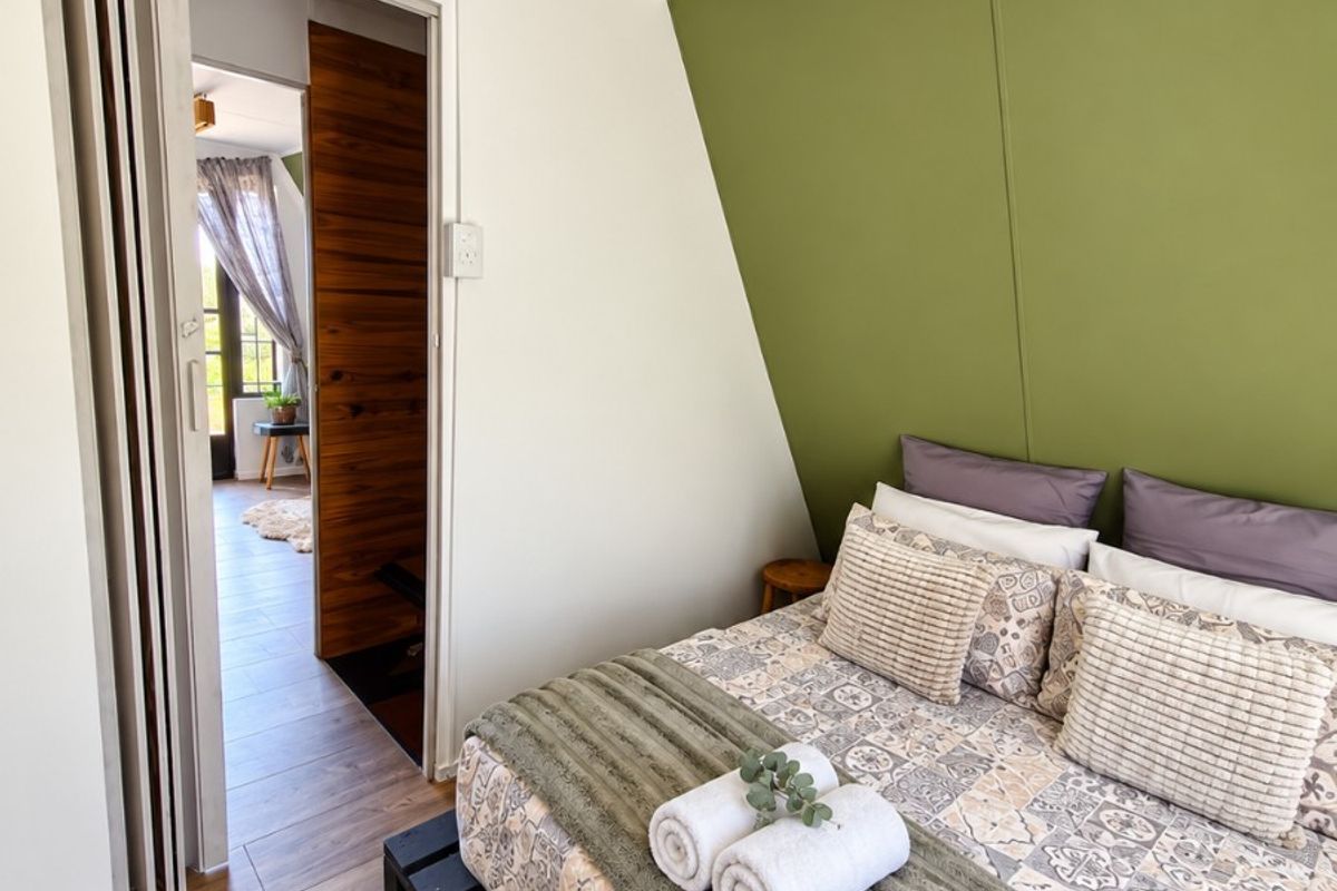 A cozy bedroom featuring laminate flooring, a distinctive green accent wall, and a space-saving folding door leading to an adjacent room.