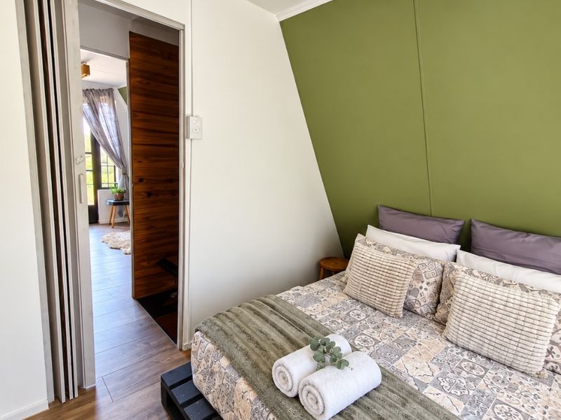 A cozy bedroom featuring laminate flooring, a distinctive green accent wall, and a space-saving folding door leading to an adjacent room.