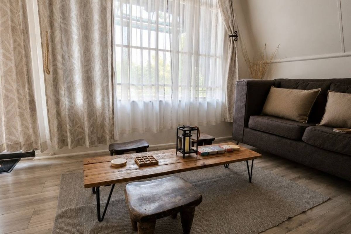 A cozy living room featuring light-toned laminate flooring, a prominent exposed timber ceiling beam, and a large window that allows for ample natural light.