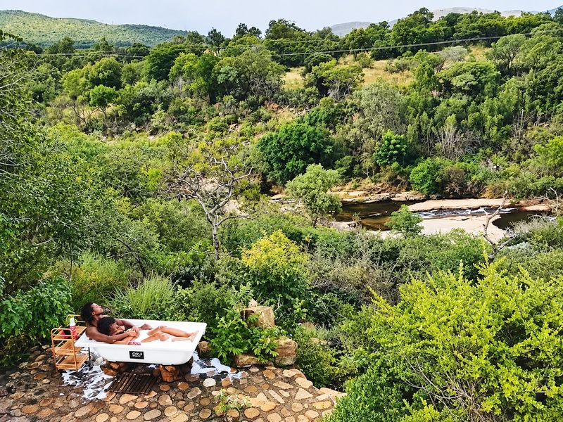 An outdoor freestanding bathtub set on a stone patio, offering scenic views of the surrounding natural landscape and river.