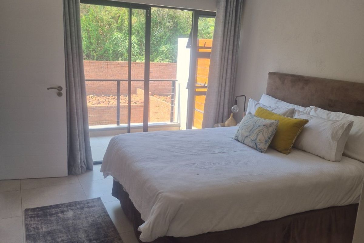 A well-lit bedroom featuring tiled flooring, a ceiling light fixture, and a sliding glass door providing access to an outdoor balcony area.