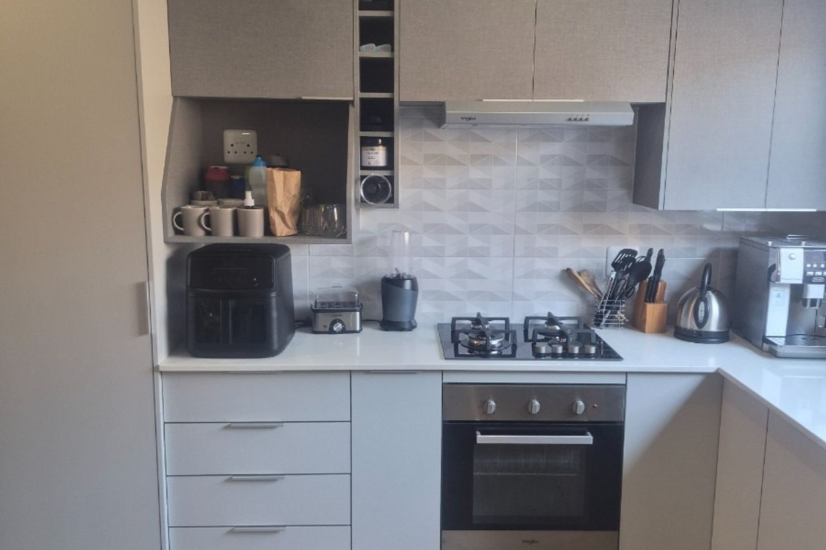 Modern kitchen featuring sleek grey cabinetry, stone countertops, a gas hob, built-in oven, and a stylish geometric tiled backsplash.