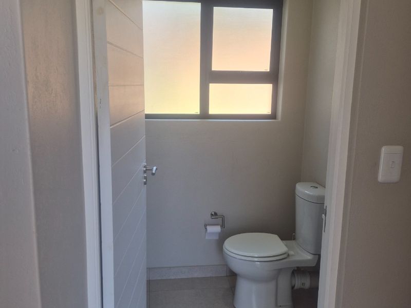 A clean and functional guest bathroom featuring tiled flooring, a modern toilet, and a frosted glass window for privacy.