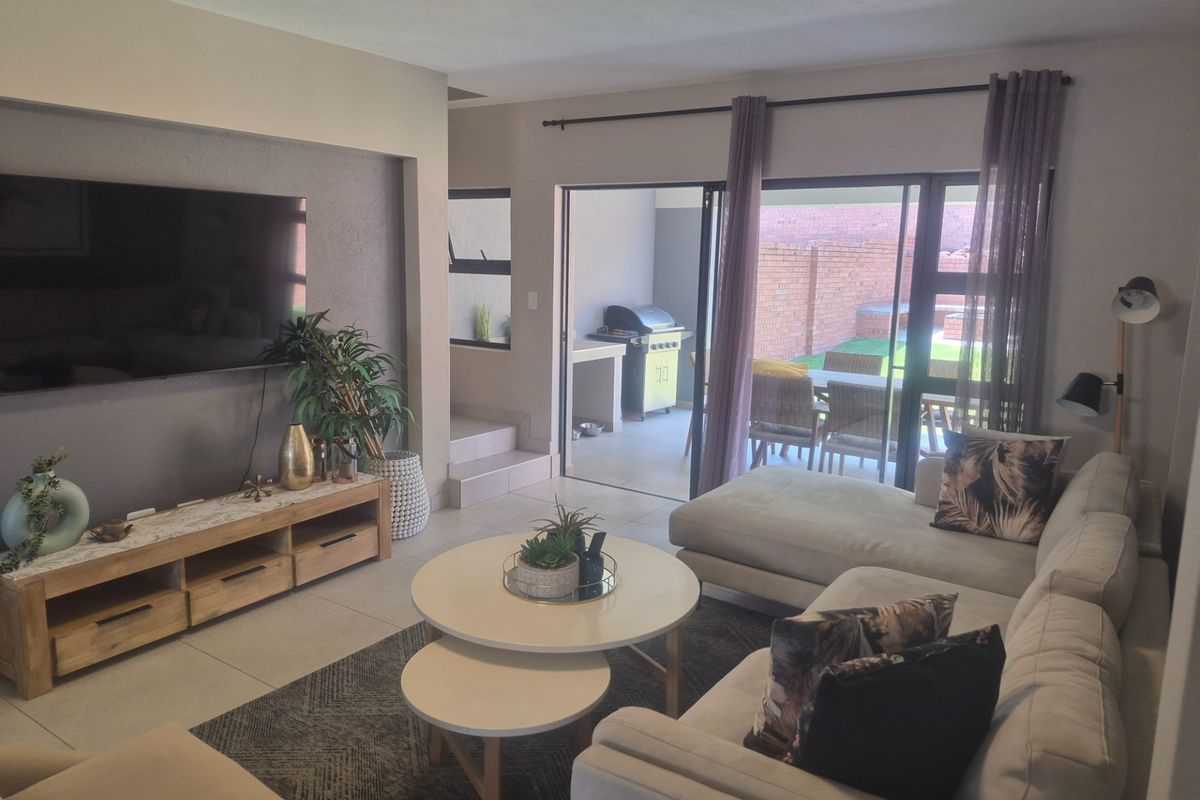 A well-maintained living room featuring tiled floors, a recessed wall niche for media, and large sliding glass doors providing access to the outdoor patio area.