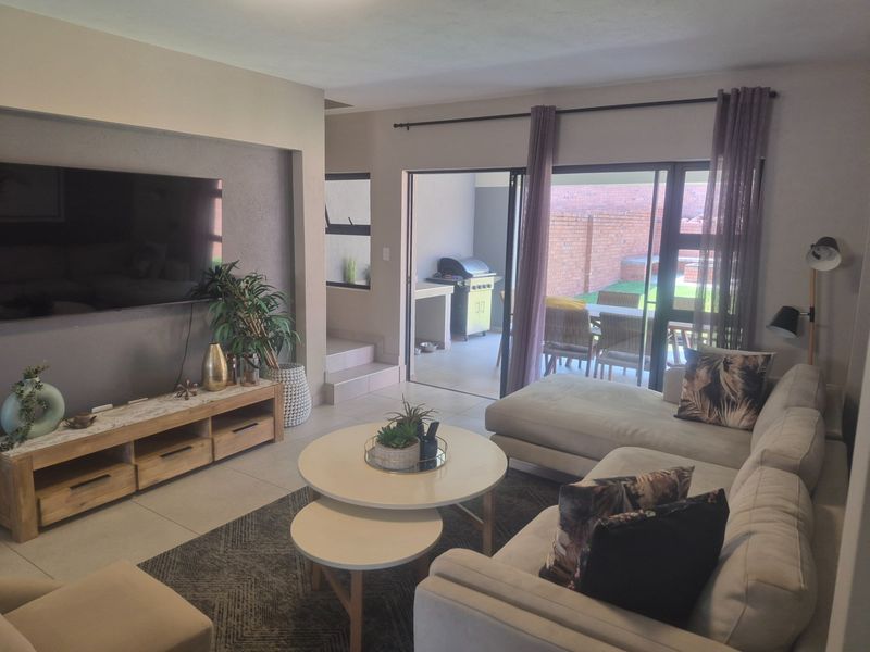 A well-maintained living room featuring tiled floors, a recessed wall niche for media, and large sliding glass doors providing access to the outdoor patio area.