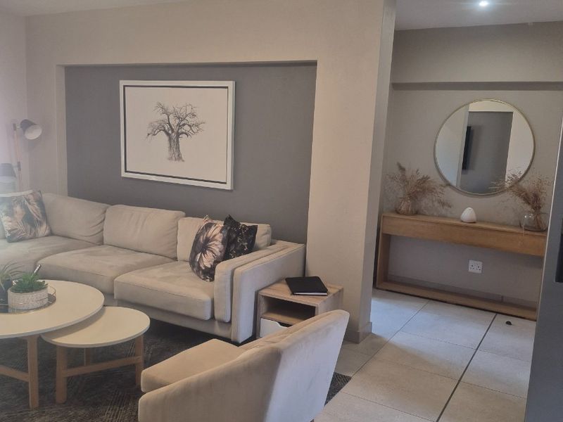 A well-maintained living room featuring neutral tiled flooring, a recessed ceiling light, and a modern grey accent wall.