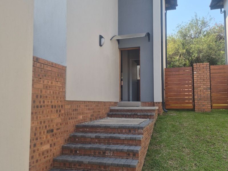 A well-maintained rear exterior view featuring a brick staircase, paved walkway, and timber privacy fencing leading to a side entrance.