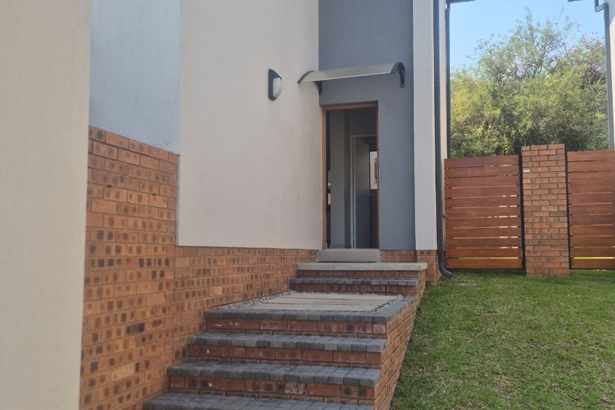 A well-maintained rear exterior view featuring a brick staircase, paved walkway, and timber privacy fencing leading to a side entrance.