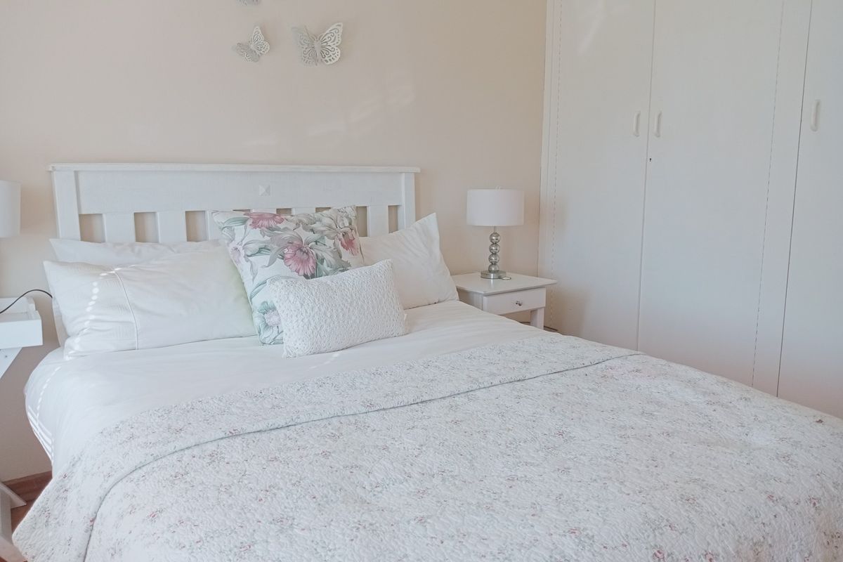 A bright bedroom featuring a built-in wardrobe with white cabinetry and neutral wall finishes.