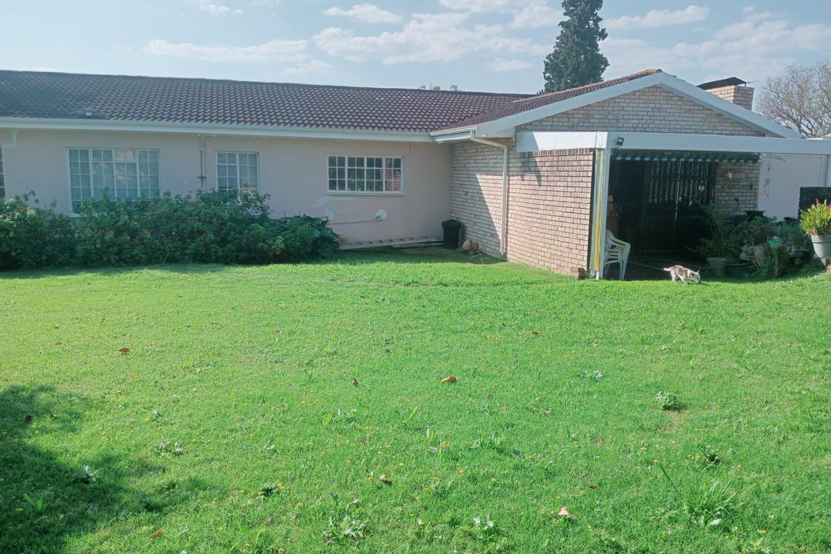 Rear view of the house featuring a brick and painted facade, a covered patio area, and a spacious grass lawn.