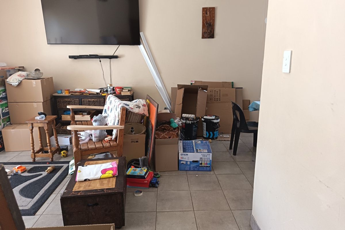 A living room area featuring tiled flooring and a wall-mounted television, currently used for storage with various boxes present.