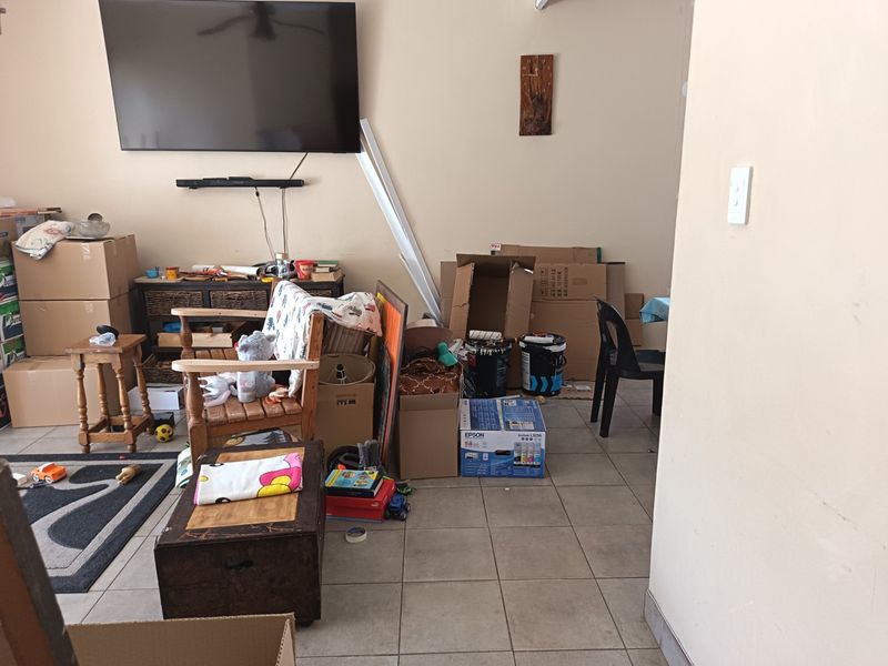 A living room area featuring tiled flooring and a wall-mounted television, currently used for storage with various boxes present.