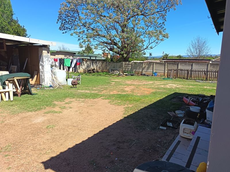 Spacious rear garden featuring a large tree, precast concrete boundary walls, and a concrete patio area, offering significant potential for landscaping and outdoor improvement.