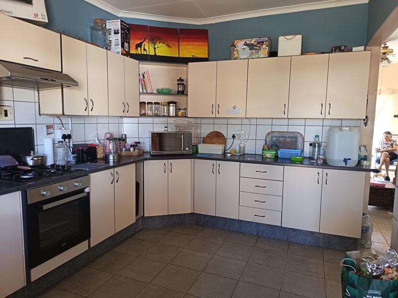 A functional kitchen featuring cream-colored cabinetry, dark laminate countertops, a gas hob with extractor fan, and tiled flooring.