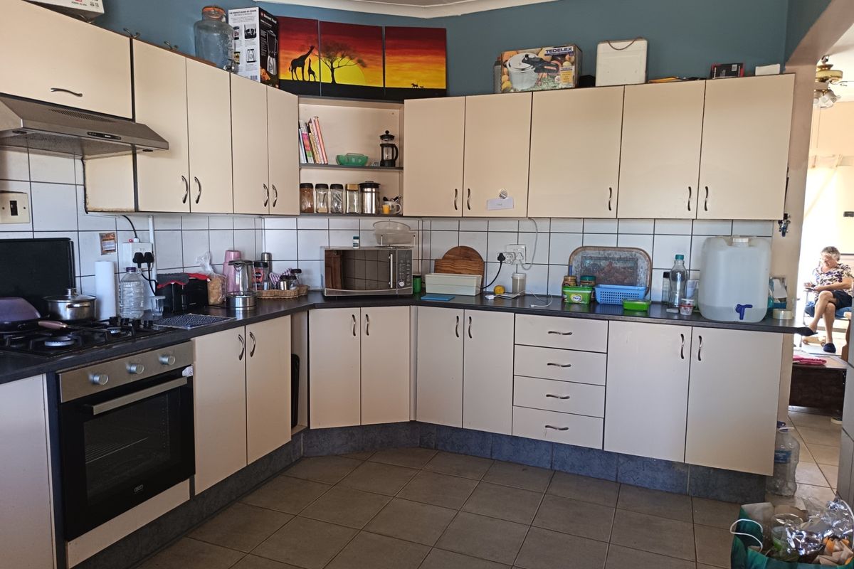 A functional kitchen featuring cream-colored cabinetry, dark laminate countertops, a gas hob with extractor fan, and tiled flooring.