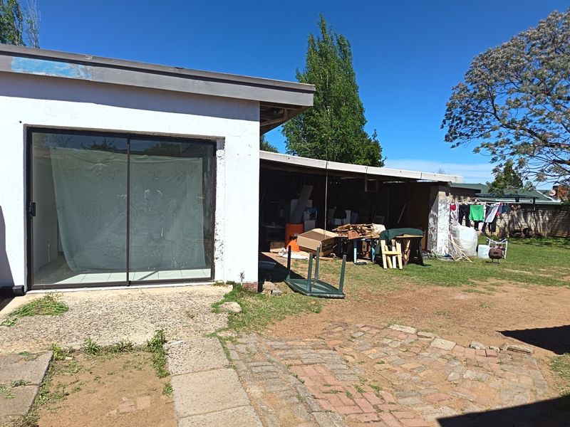 Rear view of the property featuring a covered patio area, sliding glass doors, and a paved garden space requiring maintenance.