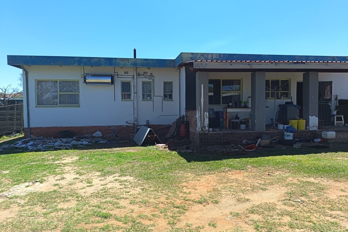 Rear view of the house featuring a covered patio area, solar water heater, and a large backyard requiring maintenance and landscaping.