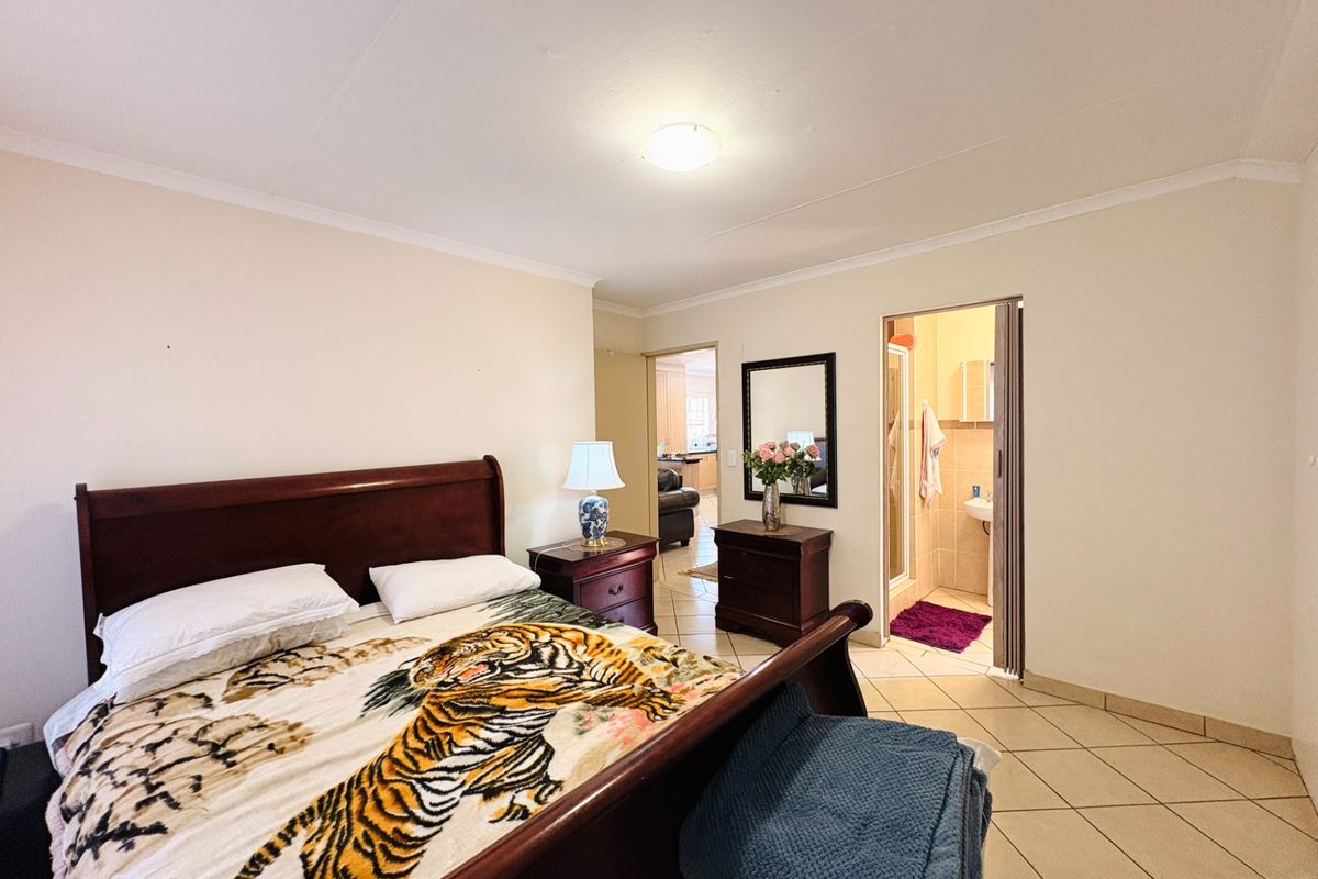 Spacious bedroom featuring tiled flooring, coving, and an attached en-suite bathroom with a folding door entrance.