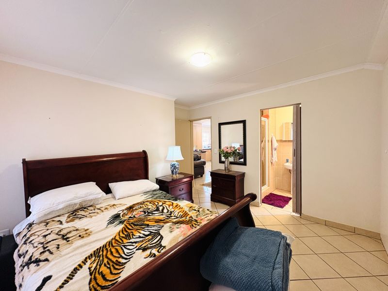 Spacious bedroom featuring tiled flooring, coving, and an attached en-suite bathroom with a folding door entrance.