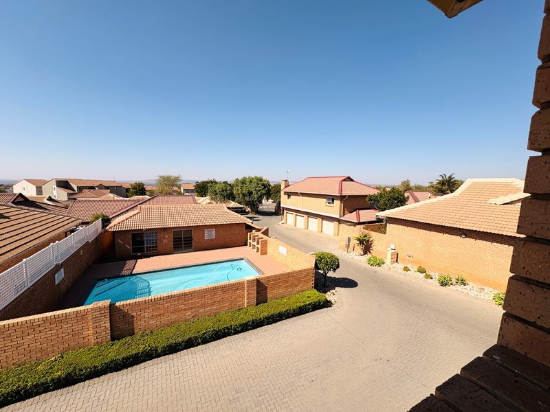 Aerial view of the apartment complex featuring a communal swimming pool, paved driveway, and brick-built residential units with tiled roofs.