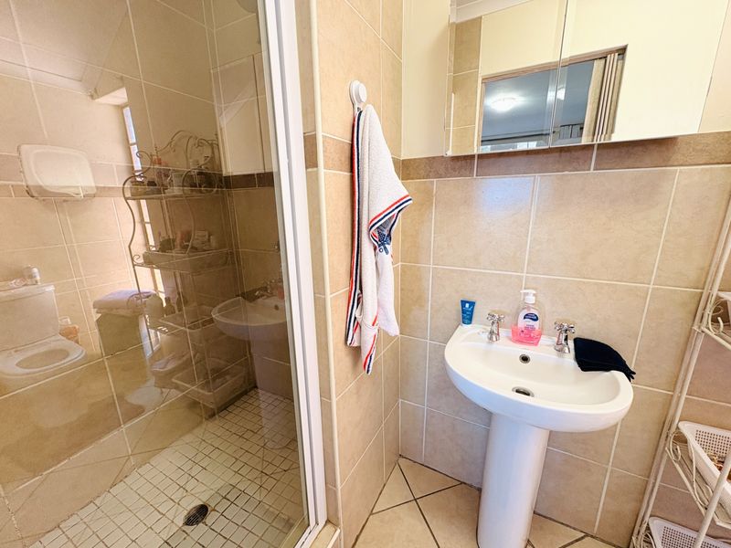 A functional bathroom featuring a pedestal basin, a glass-enclosed shower, and neutral ceramic tiling throughout.