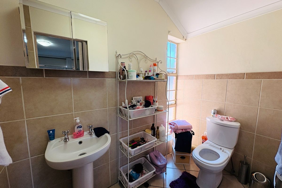 A functional bathroom featuring a pedestal basin, toilet, and mirrored medicine cabinet with neutral wall tiling and a glass block window.
