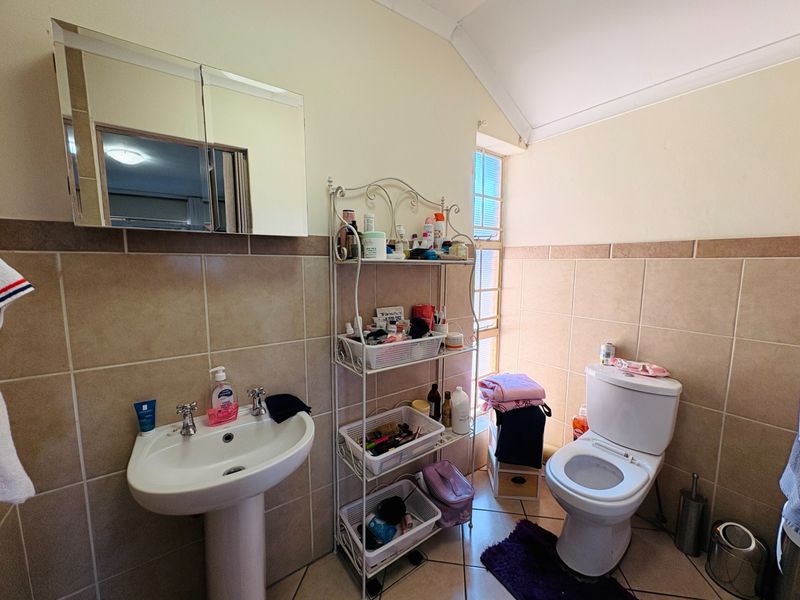 A functional bathroom featuring a pedestal basin, toilet, and mirrored medicine cabinet with neutral wall tiling and a glass block window.