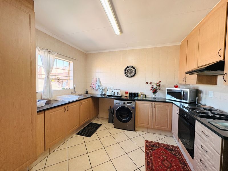 Functional kitchen featuring light wood cabinetry, granite countertops, built-in oven with gas hob, and tiled flooring with a dedicated space for laundry appliances.