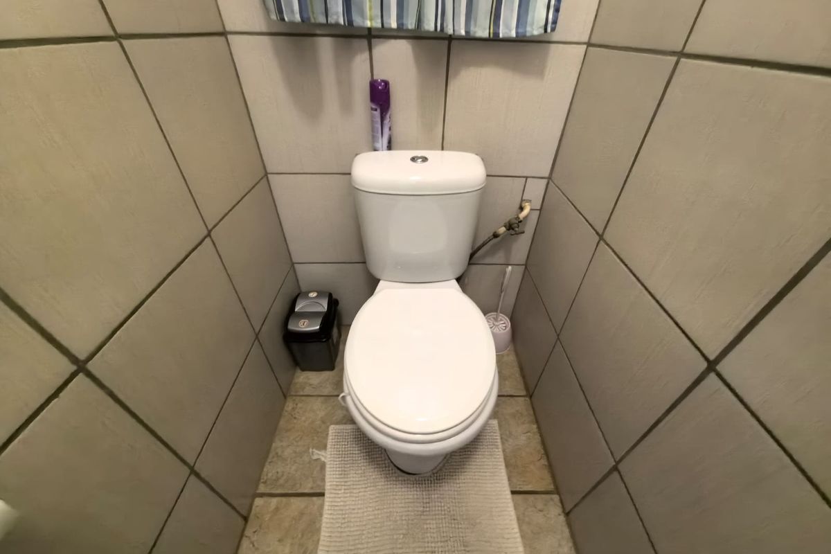 A compact bathroom featuring neutral ceramic wall and floor tiles with a standard dual-flush toilet installation.