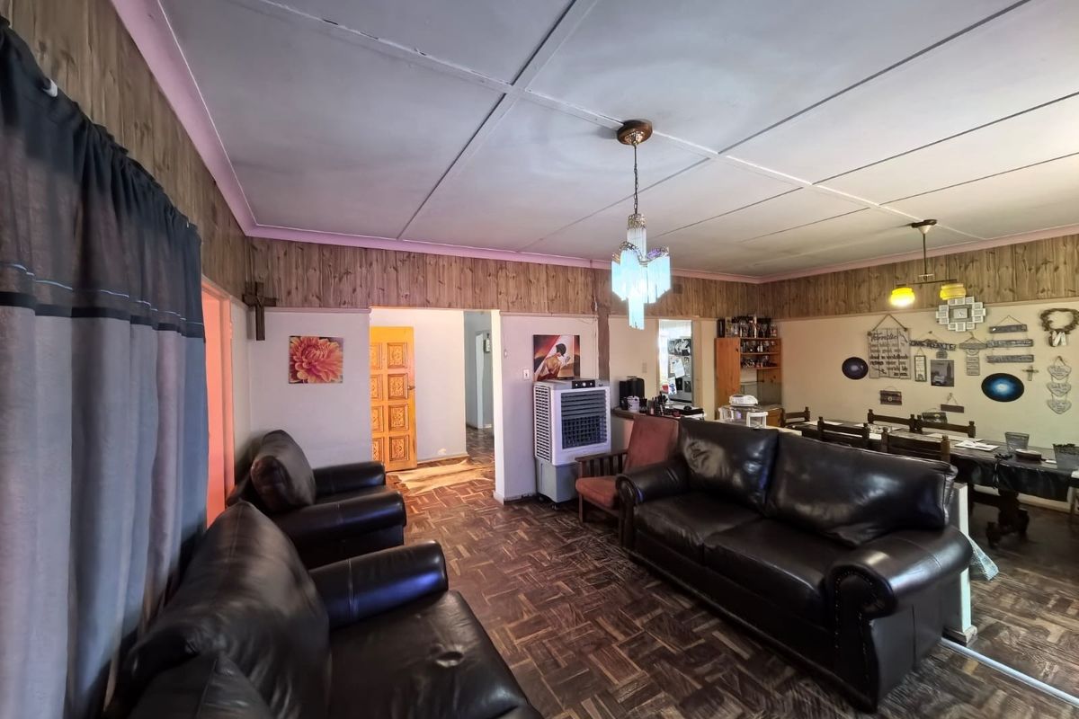 Open plan living and dining area featuring parquet flooring, wood wall paneling, and traditional ceiling tiles in a dated interior space.