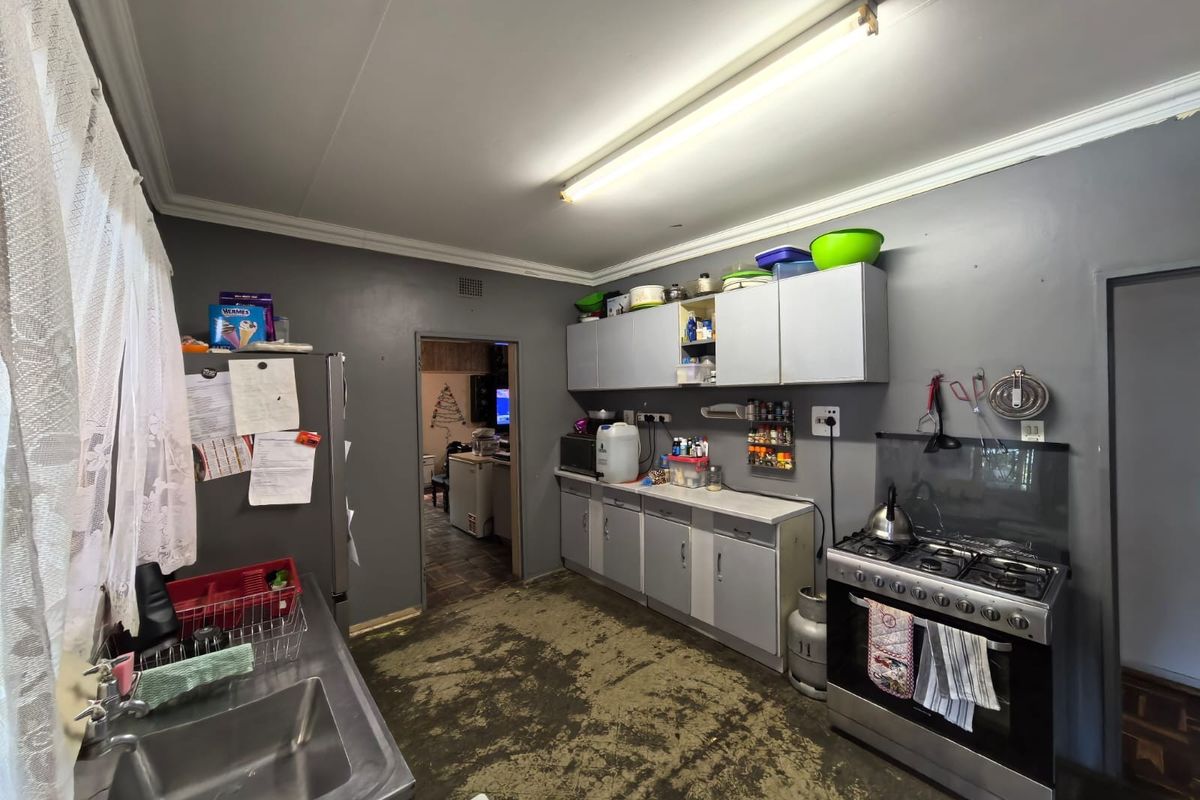 A functional kitchen featuring built-in cabinetry, a gas stove, and a stainless steel sink, requiring significant flooring and cosmetic updates.